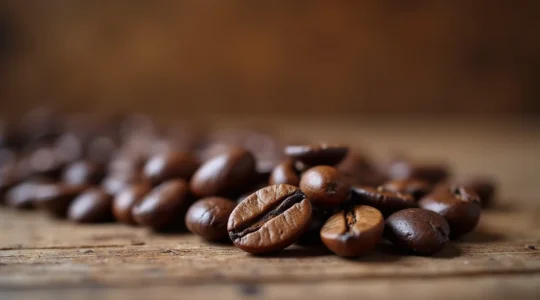 Gros plan de grains de café arabica torréfiés, étalés sur une surface en bois naturel, textures riches et détails des sillons des grains visibles